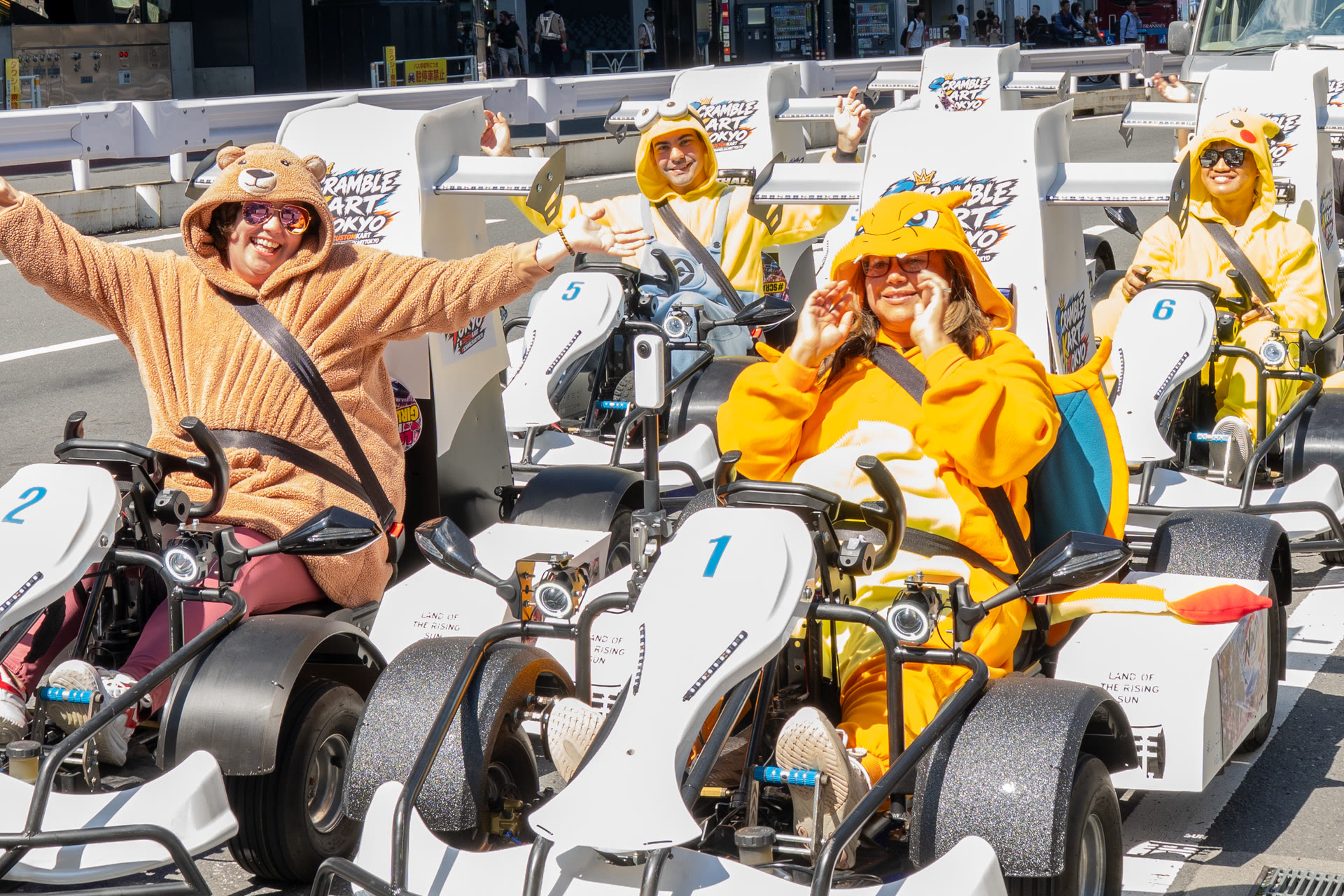 Guests in character onesies waving from a line of go-karts on a Shibuya street